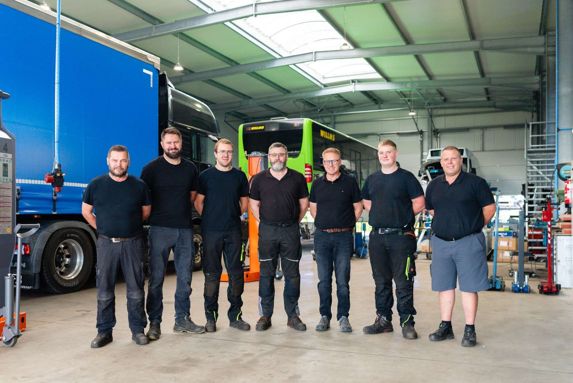 Das Team  in Arbeitskleidung posiert in einer Garage mit einem Lastwagen und einem Bus.