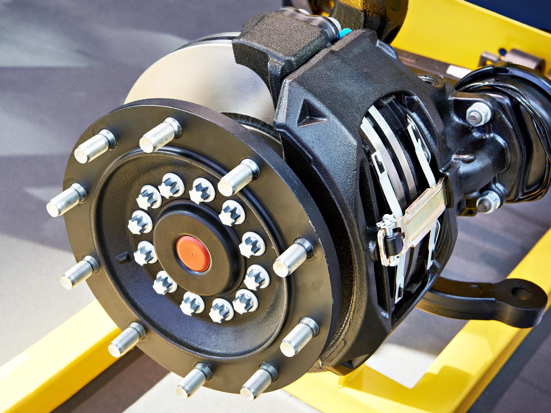 Nahaufnahme einer schwarzen LKW-Achse mit Scheibenbremse, Radbolzen und einer zentralen Nabe mit roter Kappe.