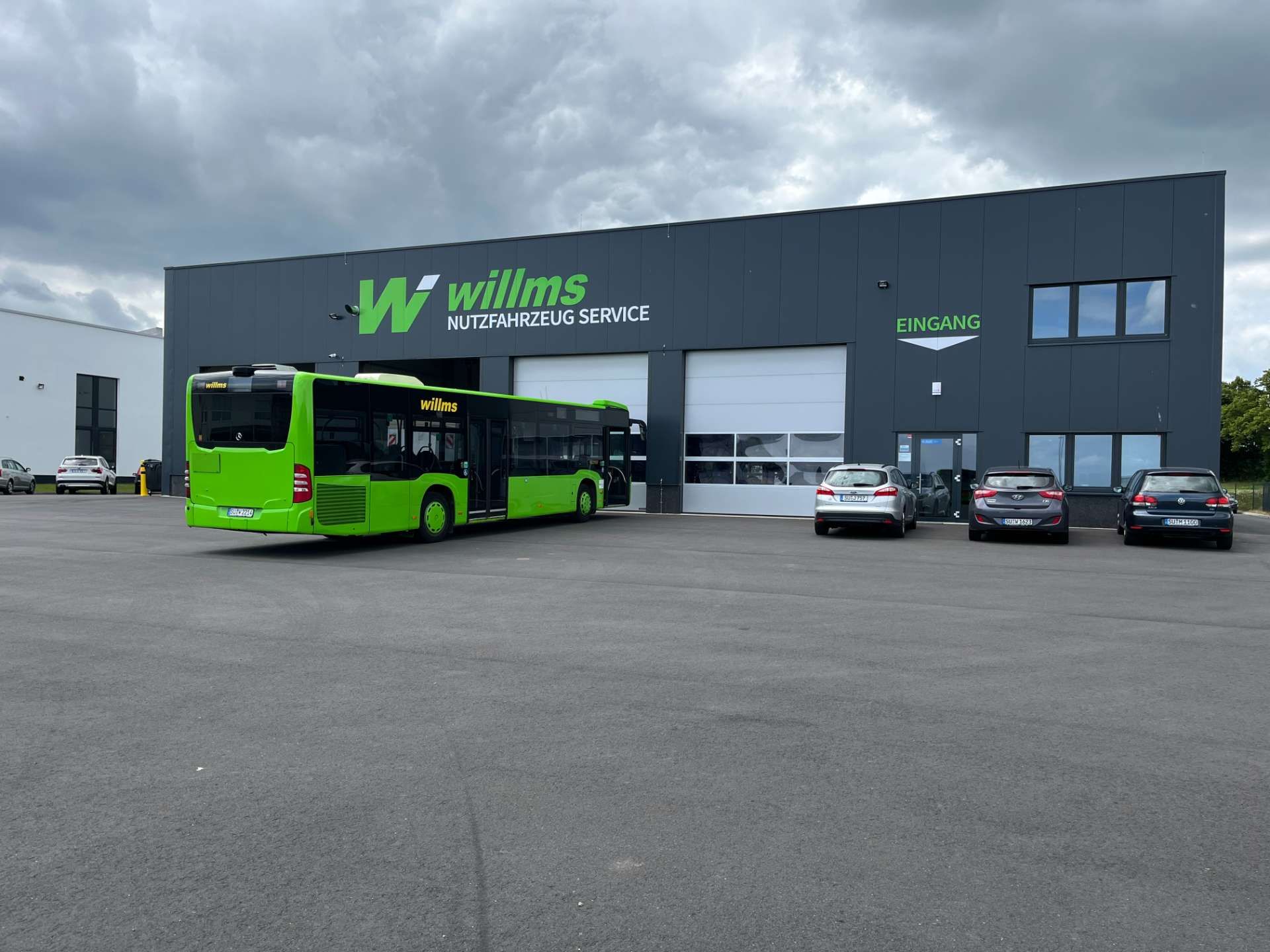 Grüner Bus  in Arbeitskleidung posiert in einer Garage mit einem Lastwagen und einem Bus.