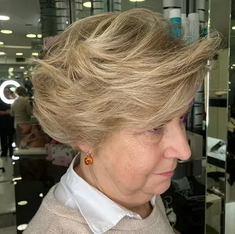 Una mujer con cabello rubio lleva una camisa blanca y aretes.