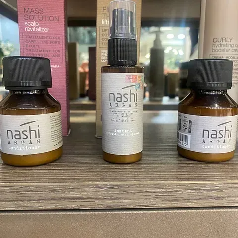 Tres botellas de productos para el cabello Nashi están sobre una mesa de madera.
