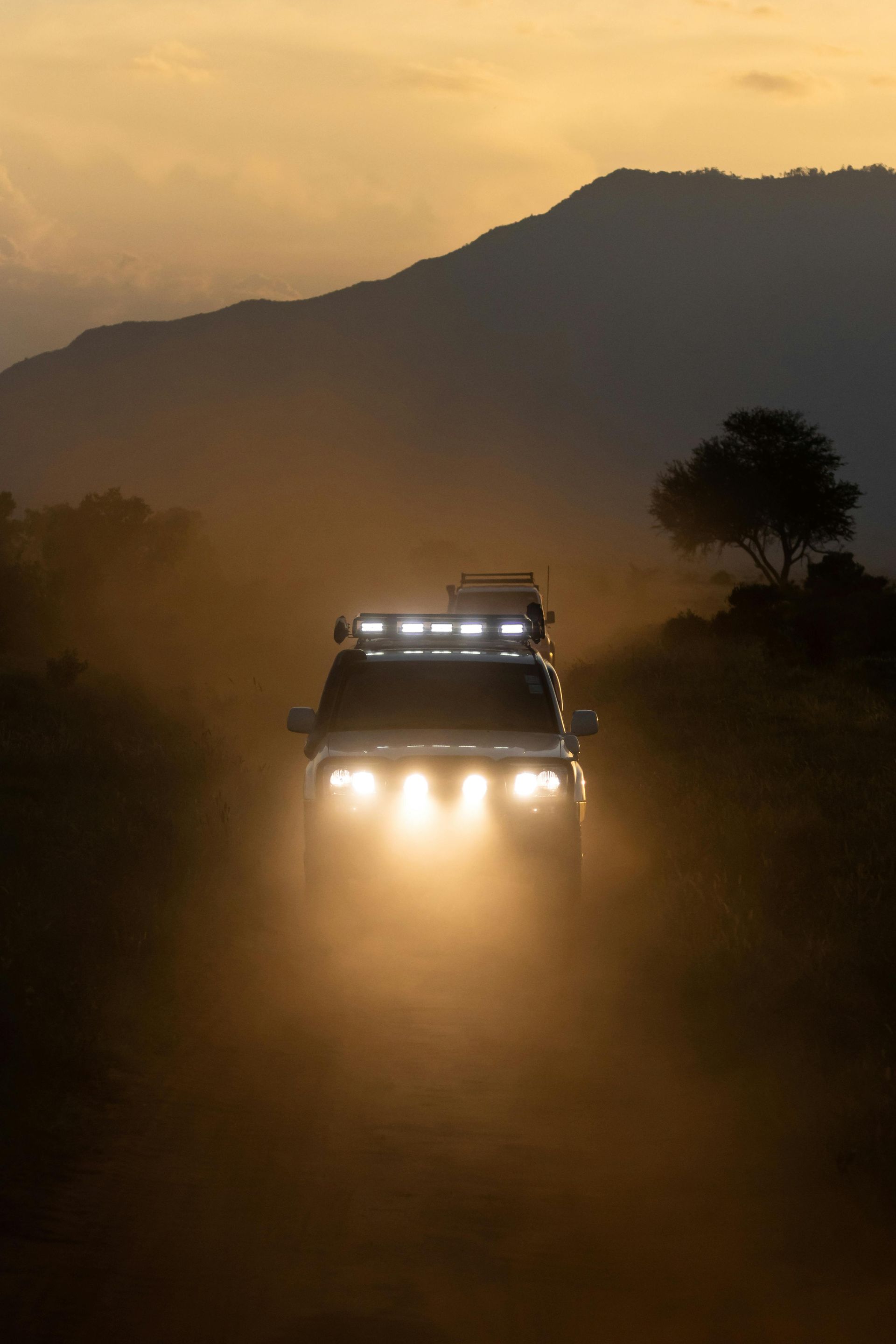 Un coche circula por un camino de tierra al atardecer.