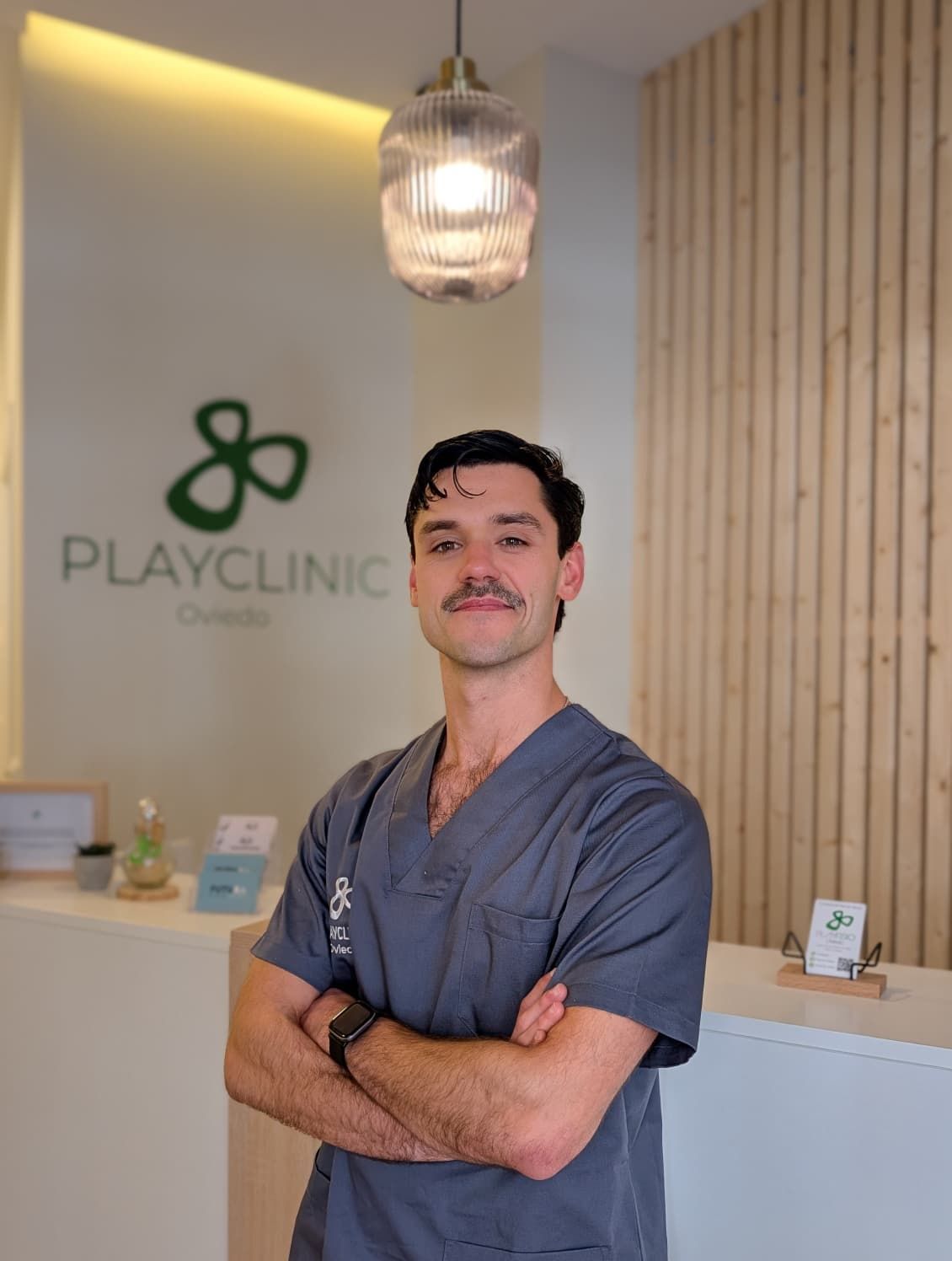 Un hombre con uniforme negro permanece sonriente frente a un logo que dice