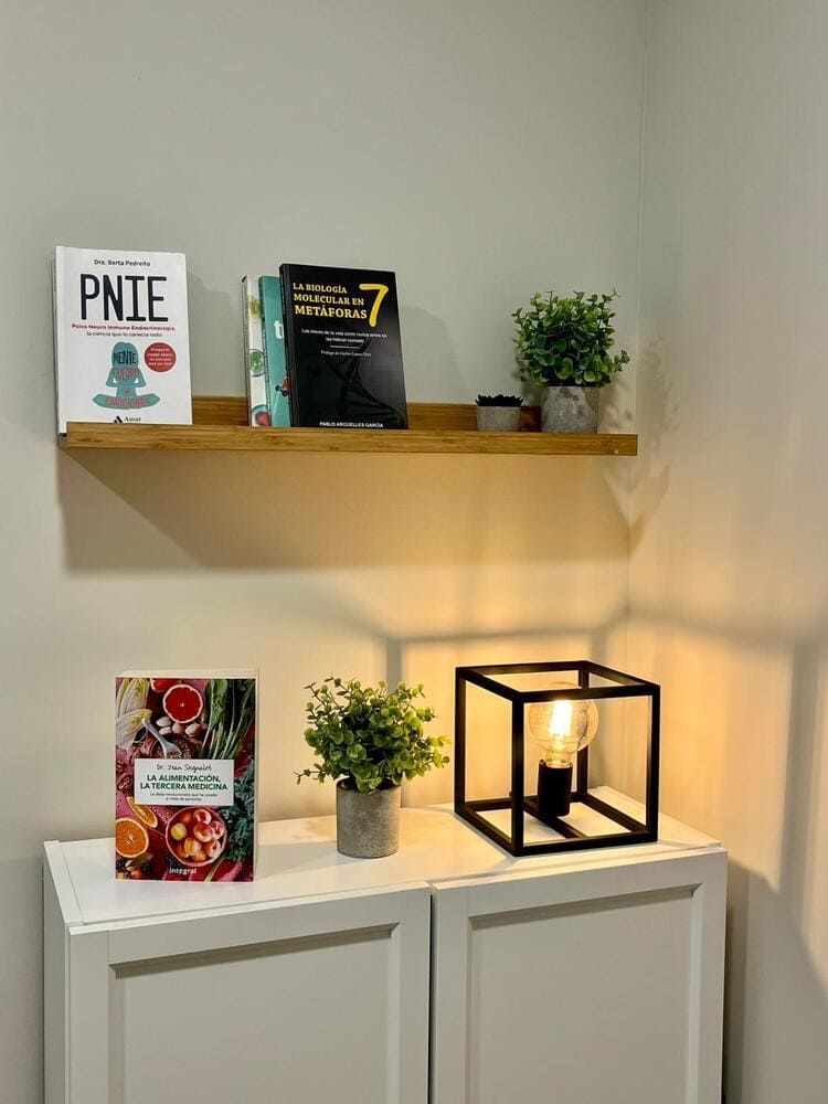 Un hombre ayuda a otro con un ejercicio de tobillo usando una banda de resistencia roja contra una pared blanca.