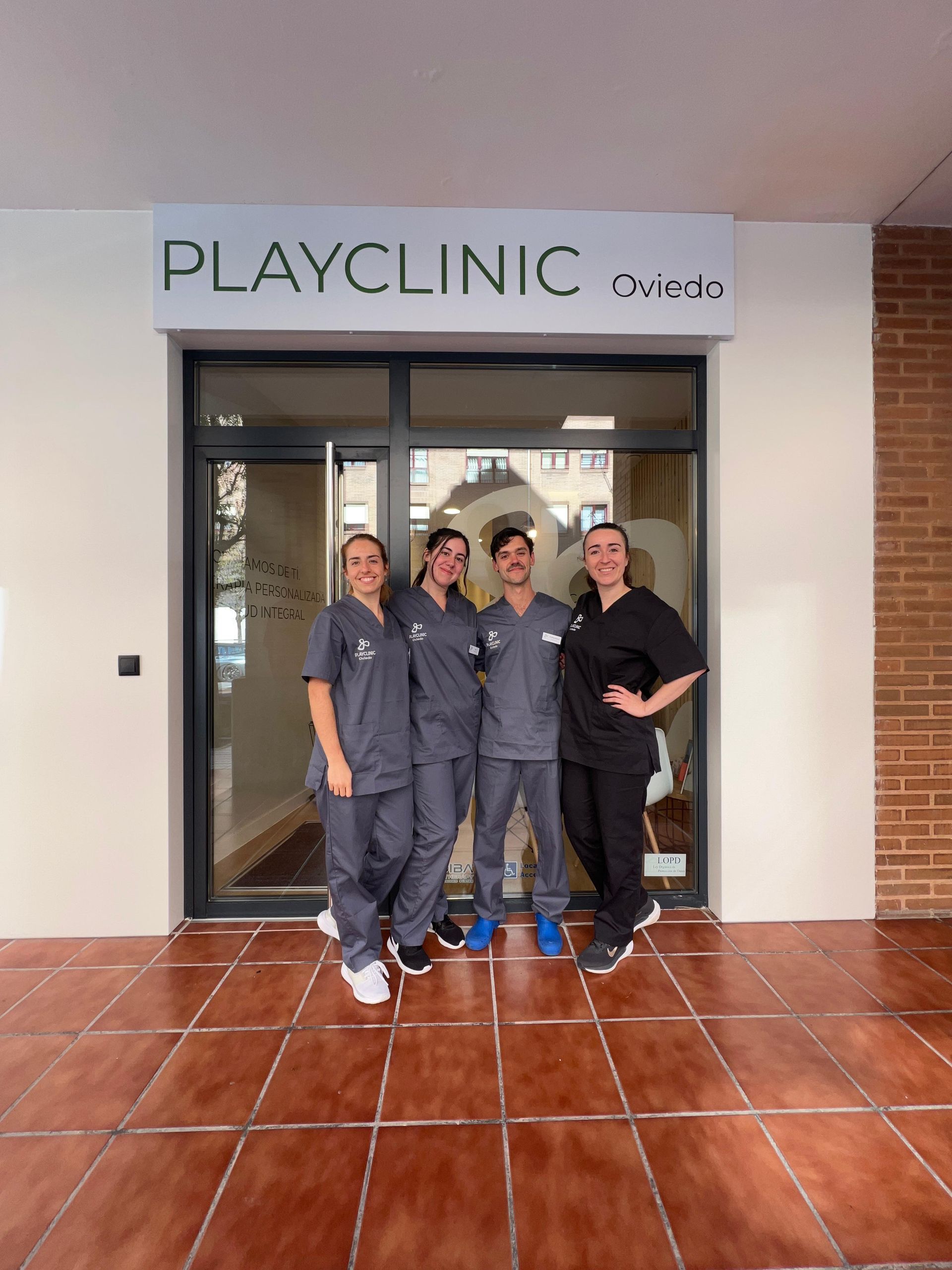 Cuatro personas frente a un logo. Tres llevan uniforme negro, una camisa blanca y vaqueros, todas sonriendo.