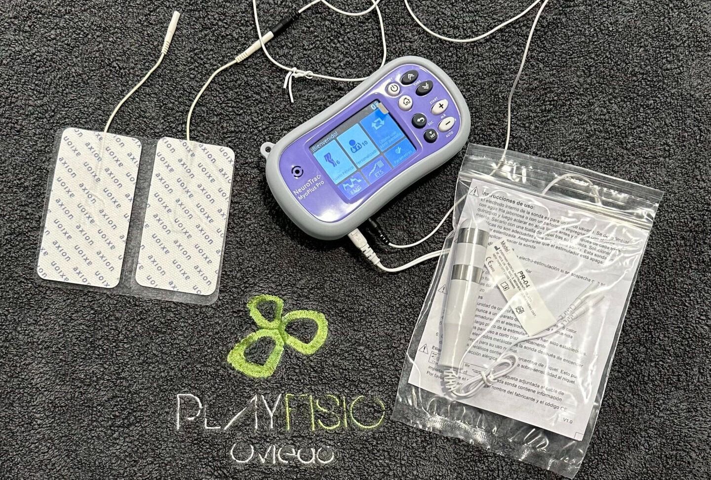 El dispositivo médico, Playnsio, incluye almohadillas, electrodos y un controlador portátil sobre un fondo oscuro.