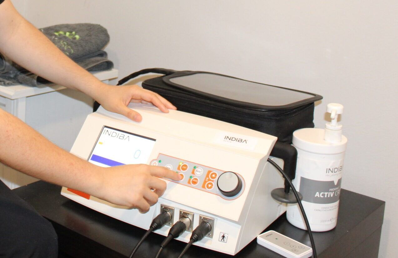 Persona operando un dispositivo médico blanco con pantalla táctil y diales. Estuche negro y frasco de gel activo cerca.