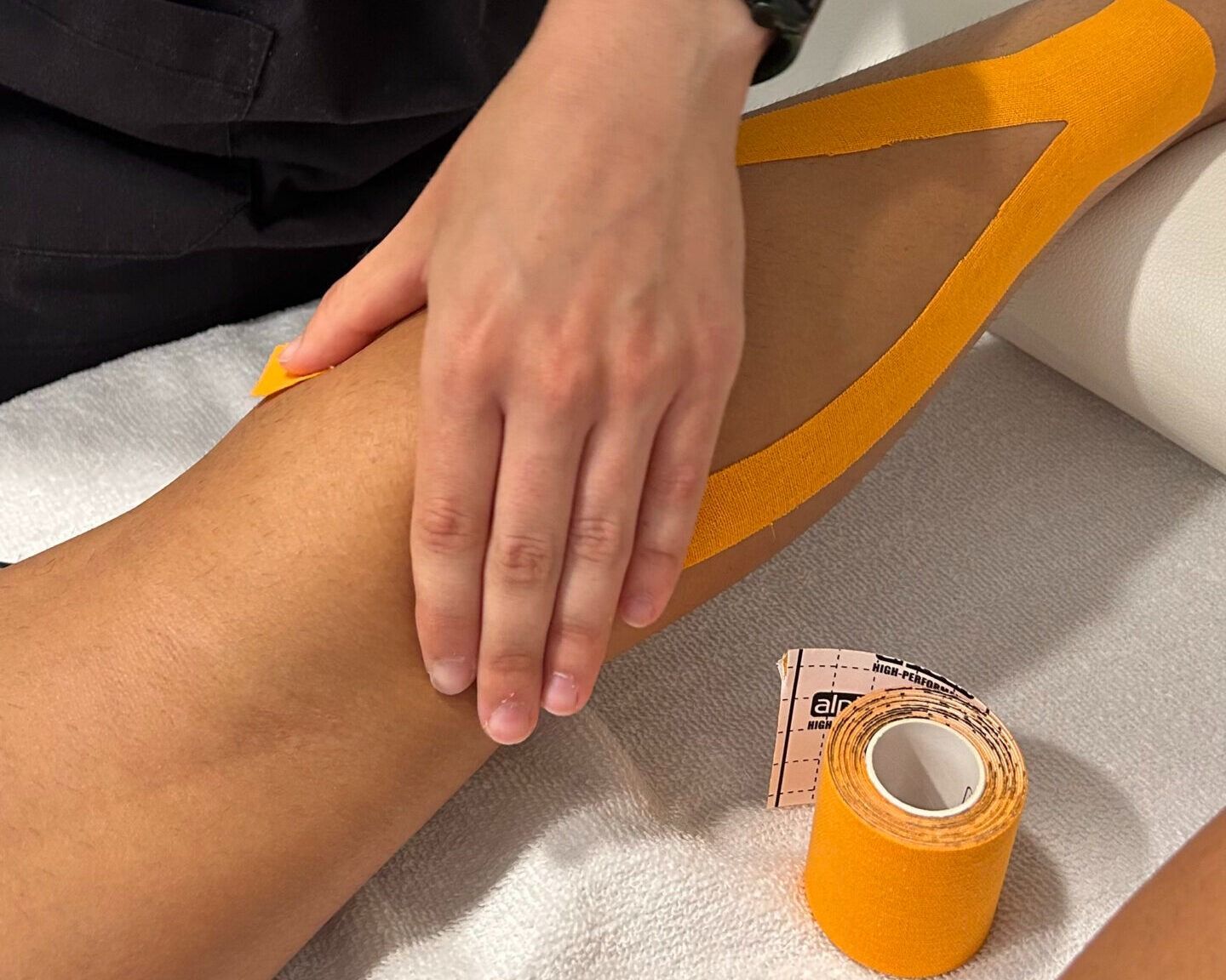 Persona que aplica cinta kinesiológica naranja en una pierna en un entorno clínico.