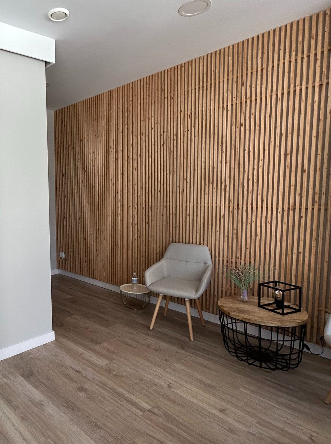 Interior de la clínica Playfisio; logotipo verde en la pared, paneles de madera, silla y mesa.