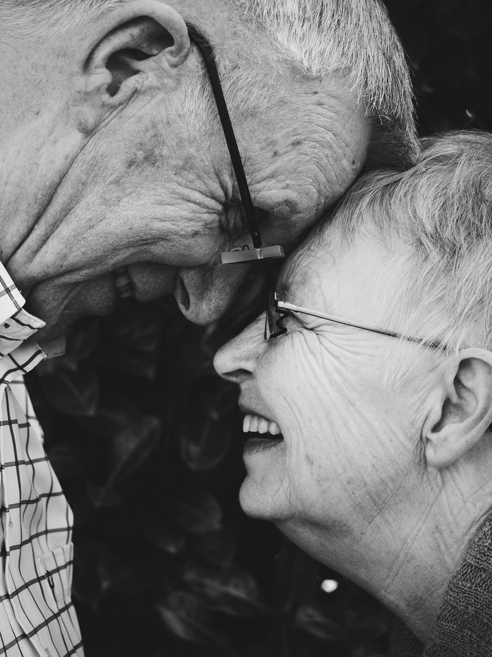 Pareja de ancianos tocándose la frente, sonriendo; blanco y negro.