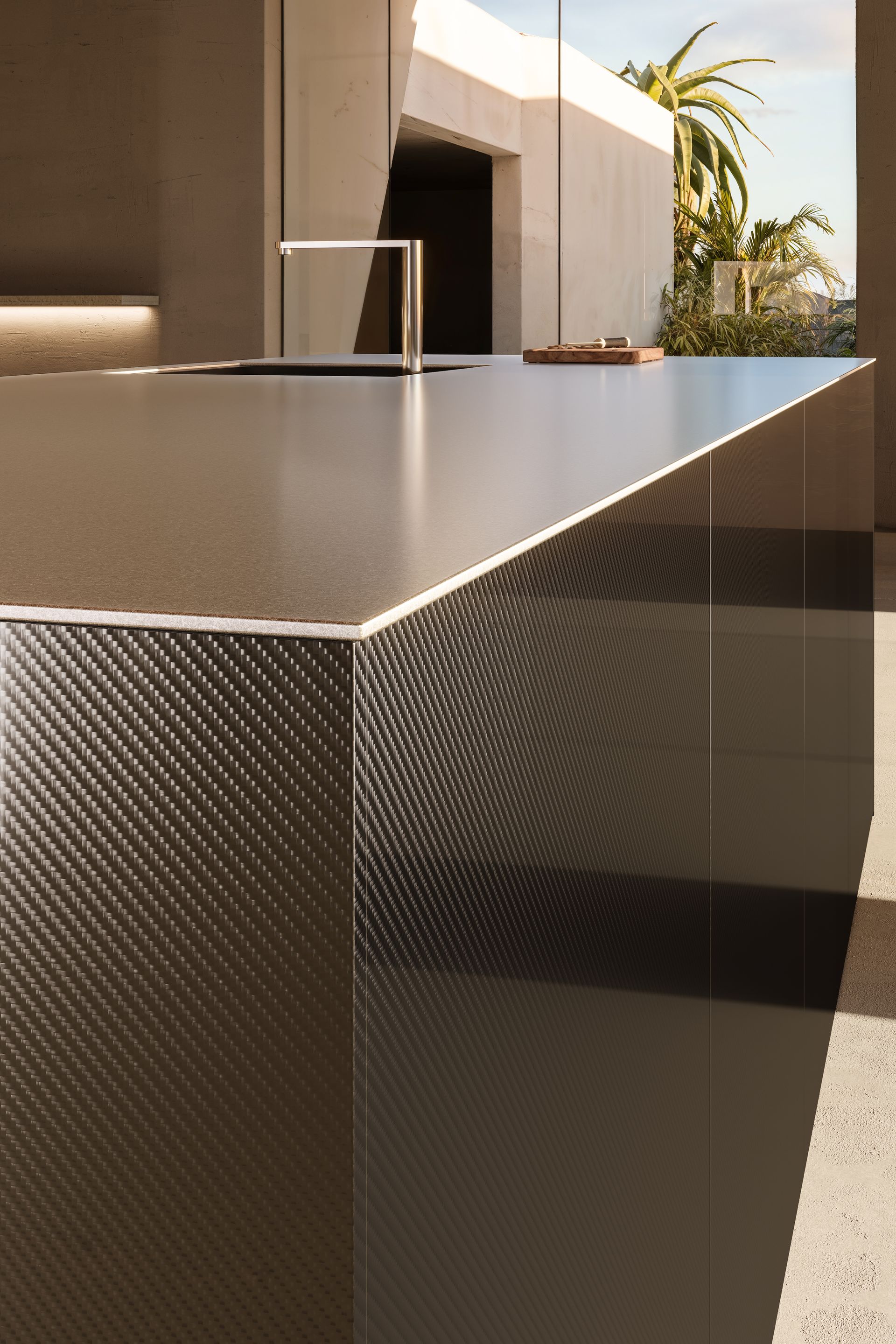 Primer plano de una isla de cocina moderna de textura oscura con una elegante encimera y grifo, ubicada al aire libre.