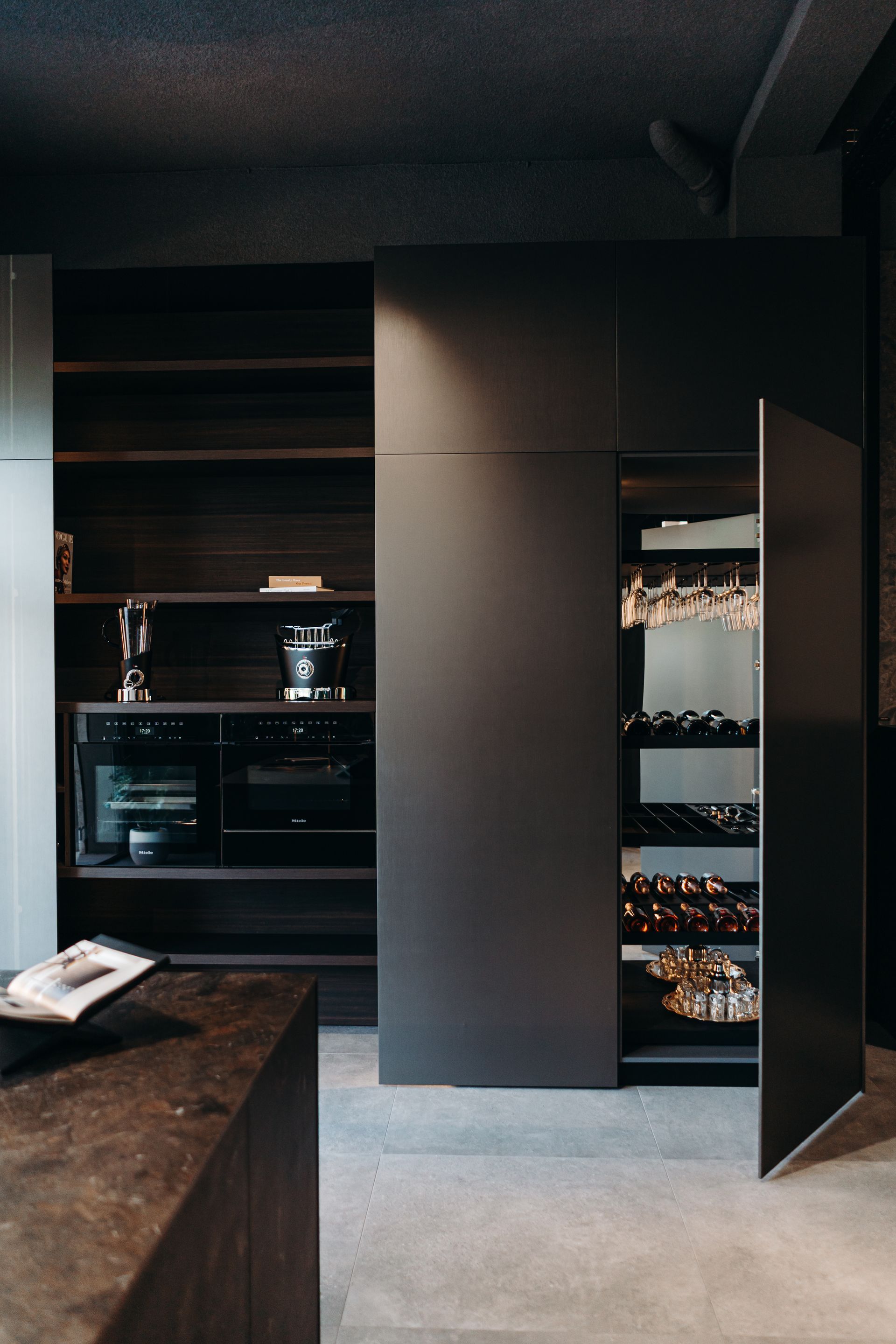 Cocina moderna oscura con electrodomésticos integrados, espacio de almacenaje y botellero.