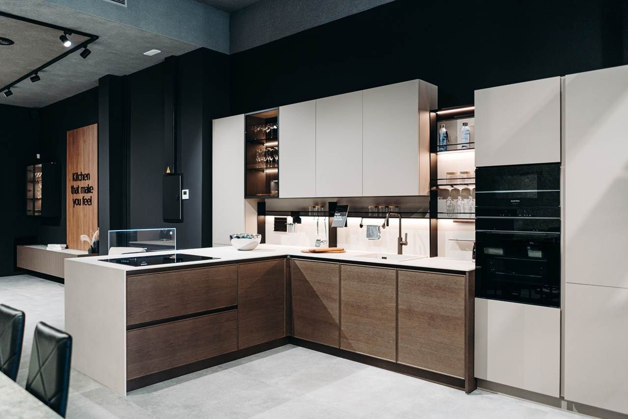 Cocina moderna con gabinetes de madera y beige claro, protector contra salpicaduras oscuro y electrodomésticos empotrados.