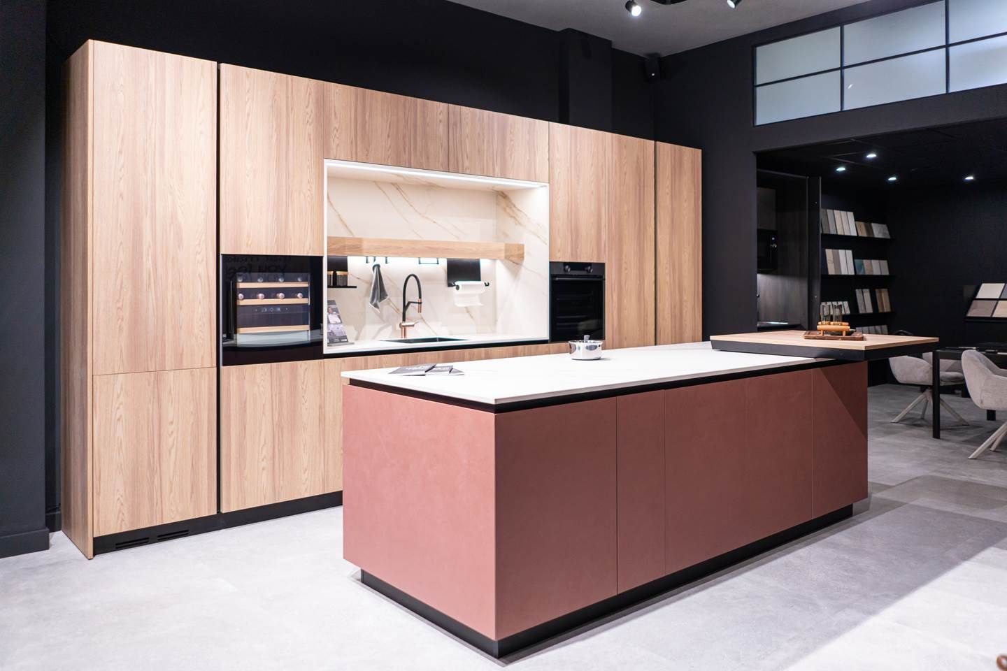 Cocina moderna con gabinetes de madera clara, isla rosa y pared con acento negro.