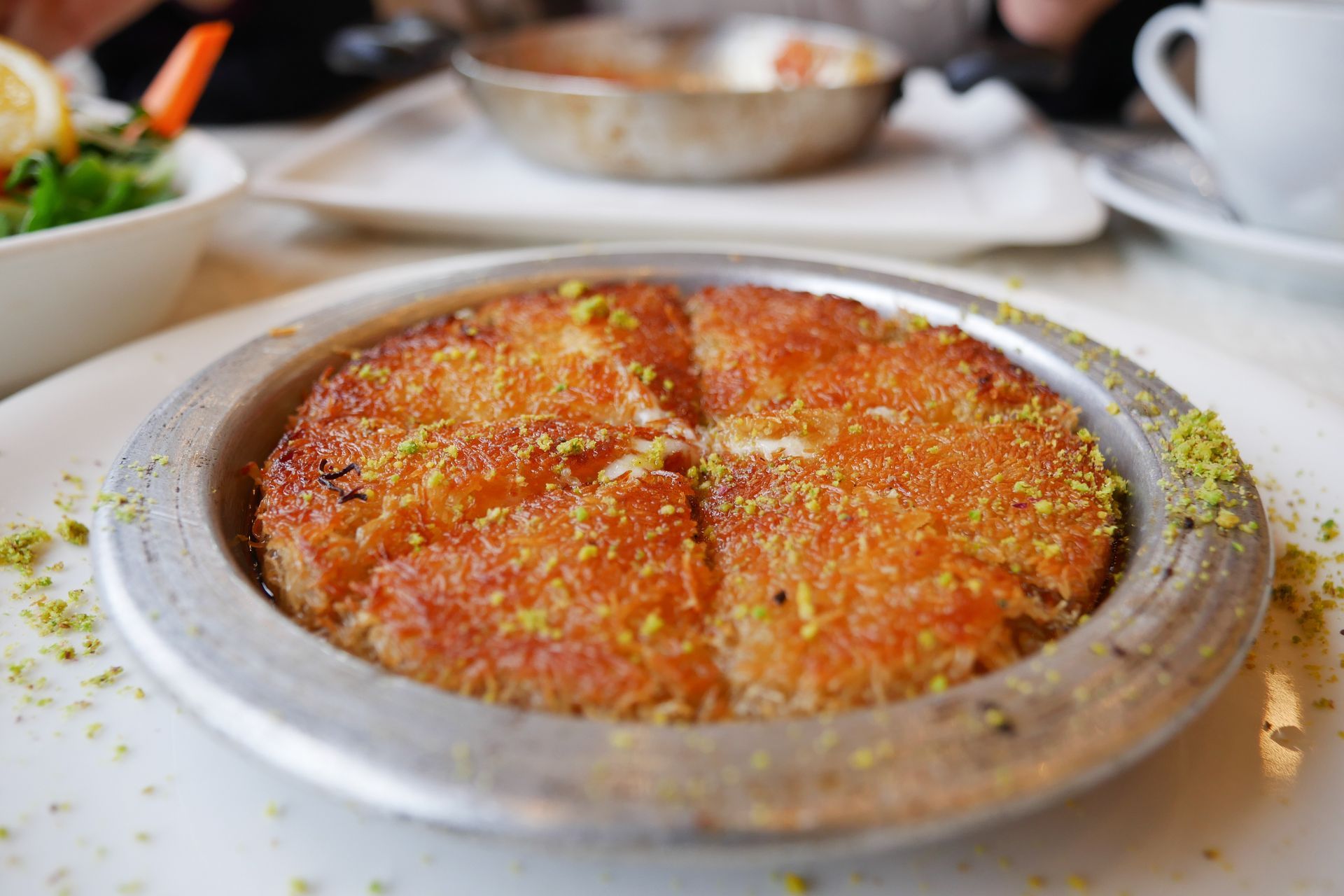 Gratin de fromage cuit au four dans un plat en métal sur une table, avec des assiettes de restaurant floues en arrière-plan