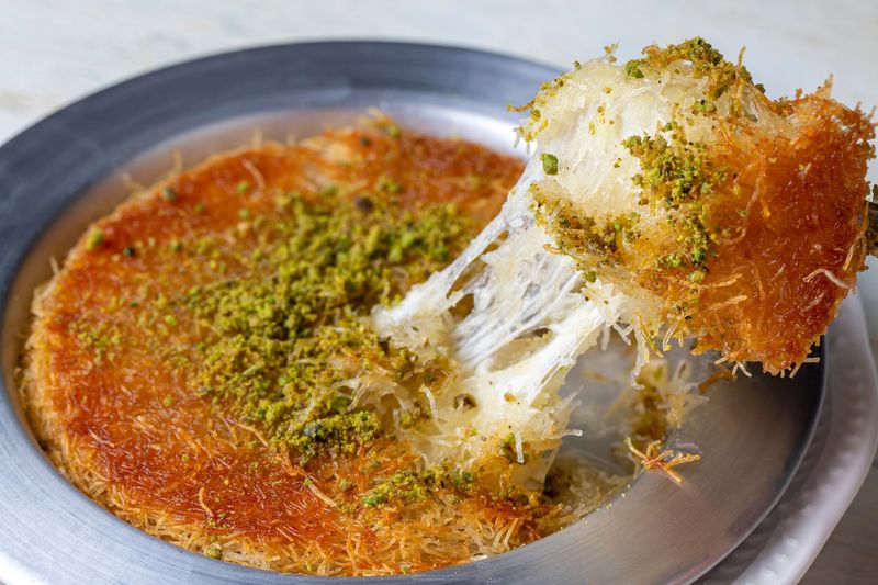 Dessert de kataifi râpé avec des miettes de pistaches et du fromage fondu sur une assiette en métal