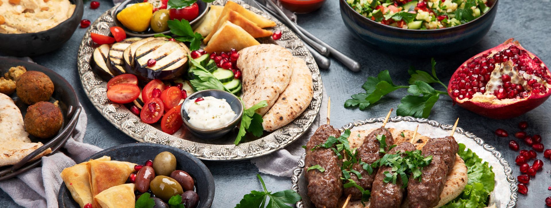 Assortiment de plats méditerranéens sur une table, comprenant du poulet grillé, des olives, de la salade, des fruits et du pain.