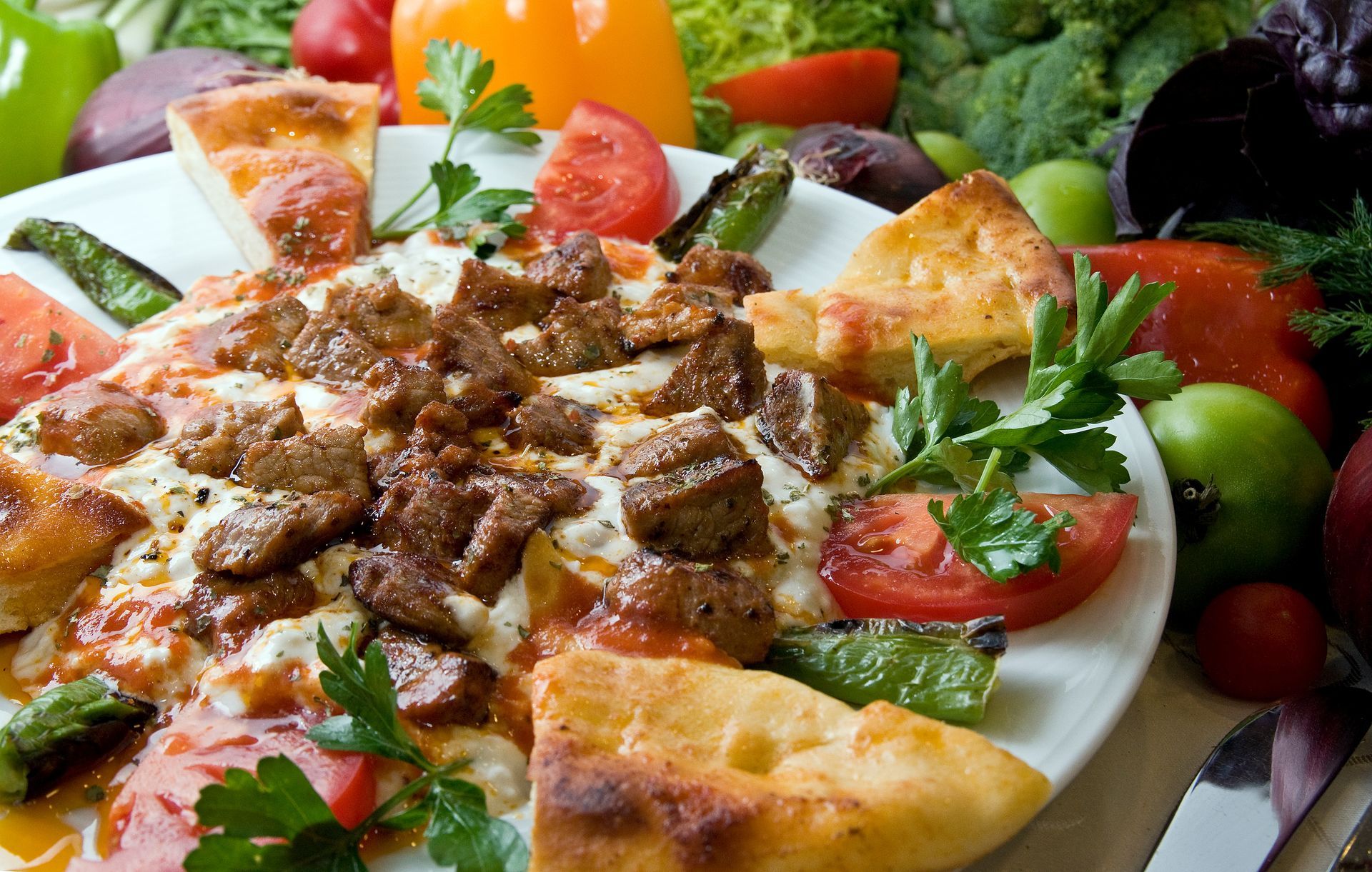 Viande grillée servie sur une table, accompagnée de quartiers de pita, de tomates, de concombres et de persil.