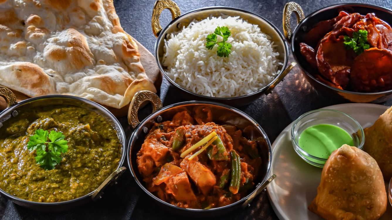 Table avec du riz, du curry, du naan, des samoussas et du chutney vert.
