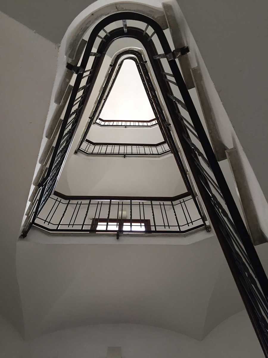 Vista hacia una escalera de caracol con barandillas de hierro forjado negro y un techo blanco.