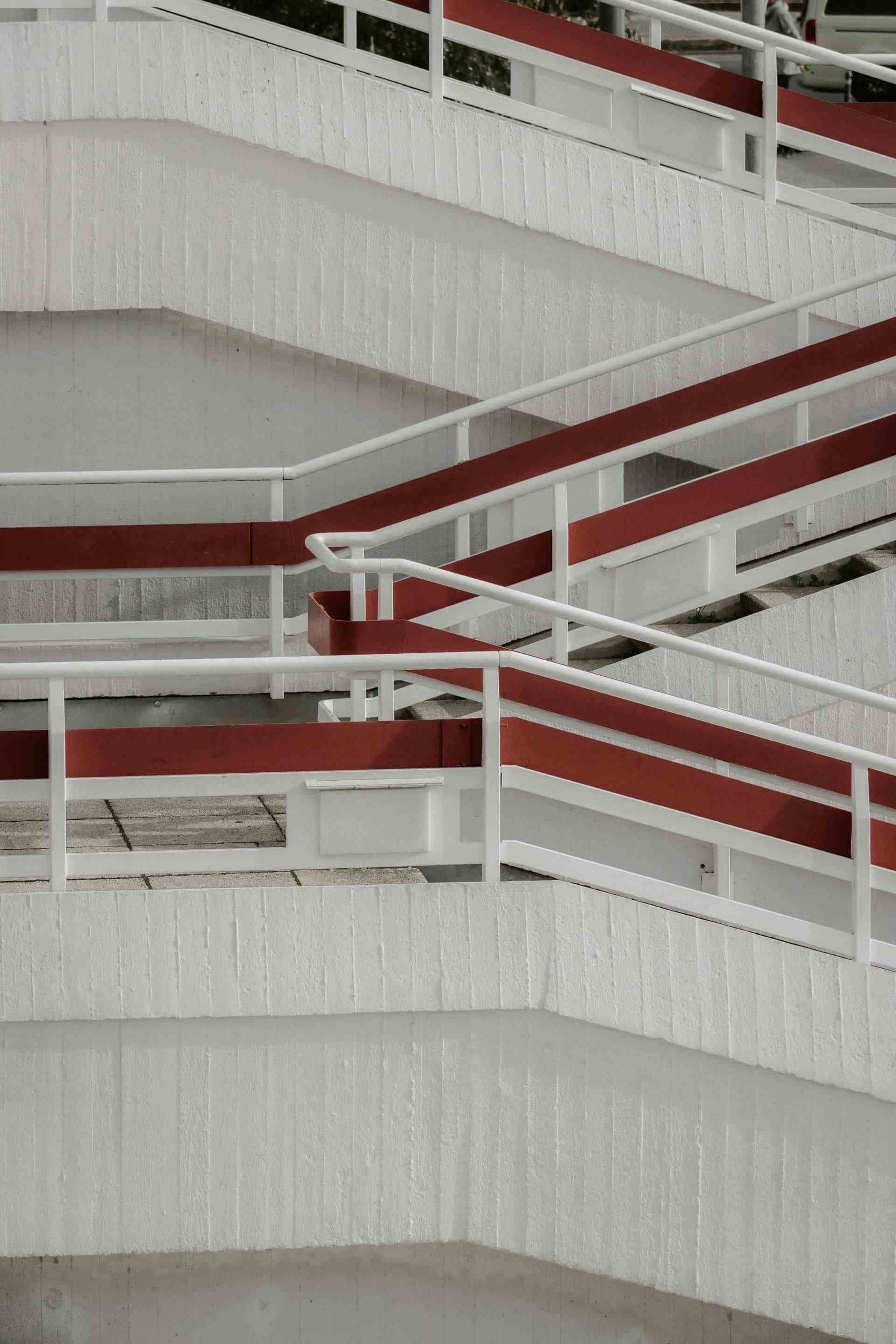 Escalera exterior de hormigón blanco con pasamanos rojos.