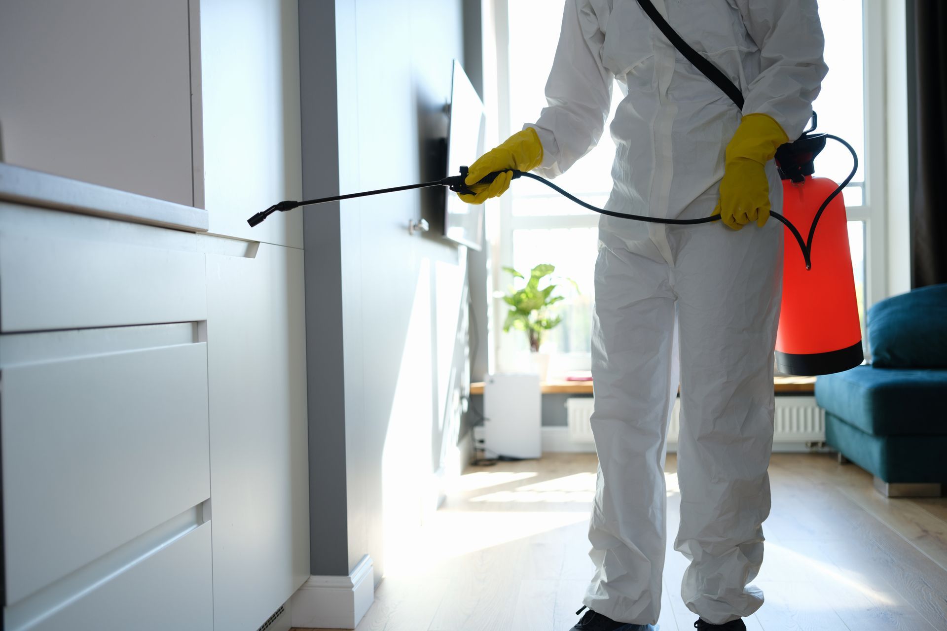 Agent de désinsectisation en combinaison blanche pulvérise un produit dans un couloir avec un réservoir dorsal rouge