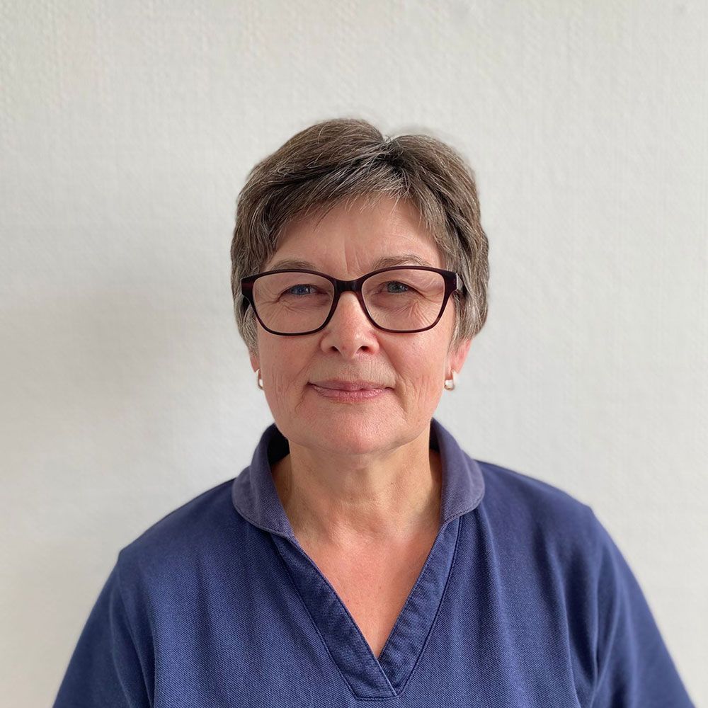 Frau mit kurzen braunen Haaren, Brille und blauem Hemd, lächelt in die Kamera.