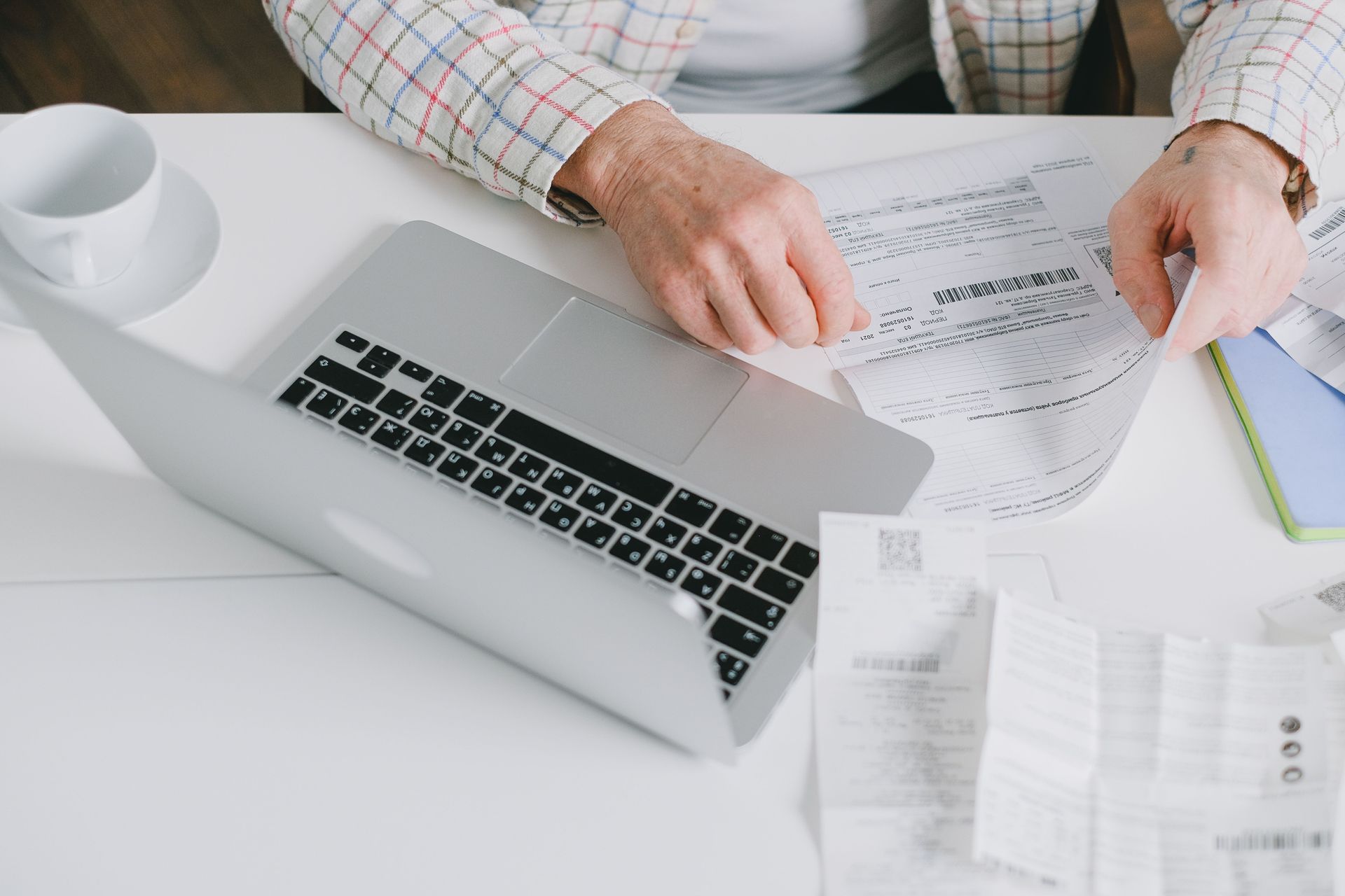 Manos revisando gráficos financieros junto a una computadora portátil sobre un escritorio blanco.
