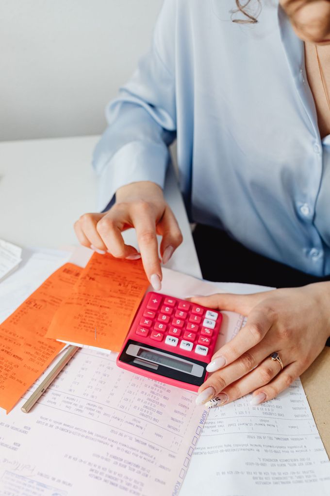 Persona usando una calculadora rosa en documentos con notas naranjas sobre un escritorio.