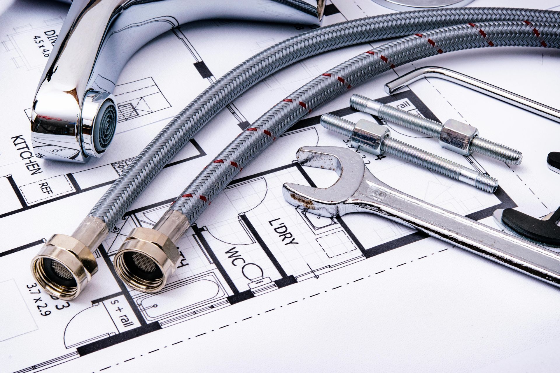 Grifo, mangueras de plomería, llaves y herramientas en un plano, indicando renovación o construcción.