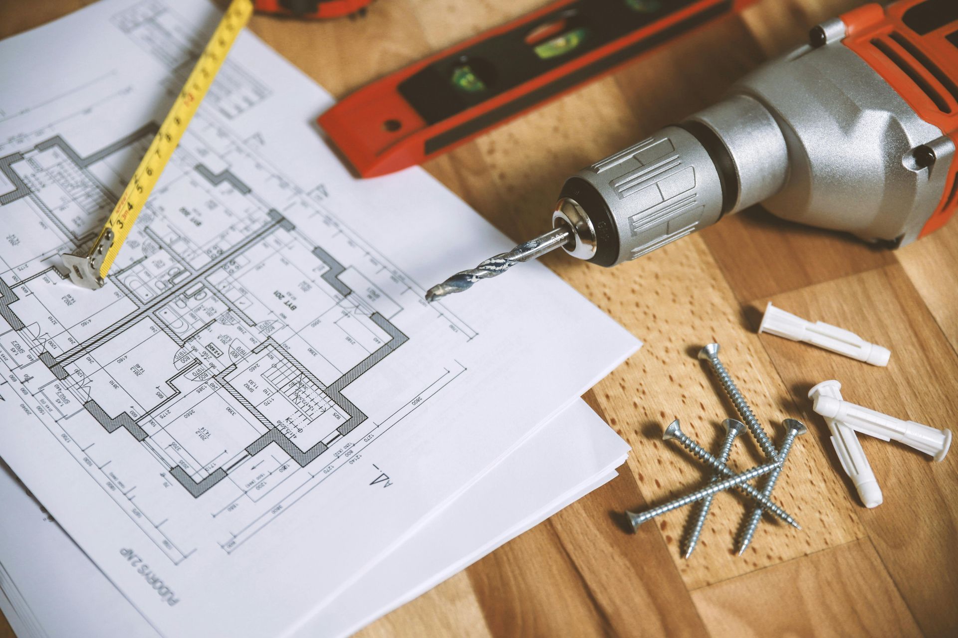 Plano, taladro, clavos y cinta métrica sobre una superficie de madera, herramientas para construcción.