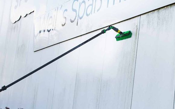 Eine Person reinigt eine weiße Wand mit einer grünen Bürste.