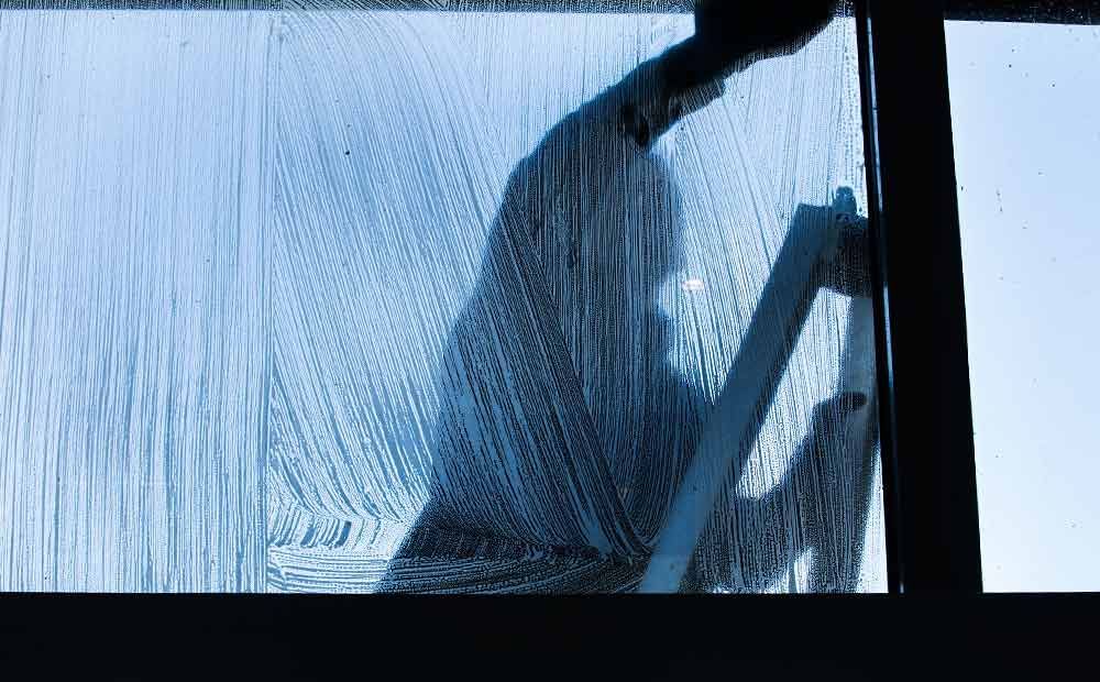 Ein Mann putzt mit einer Leiter ein Fenster.