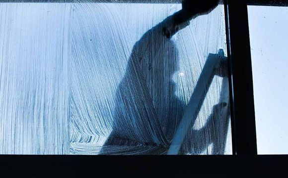 Ein Mann putzt mit einer Leiter ein Fenster.