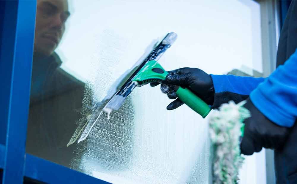 Eine Person reinigt ein Fenster mit einem Abzieher.