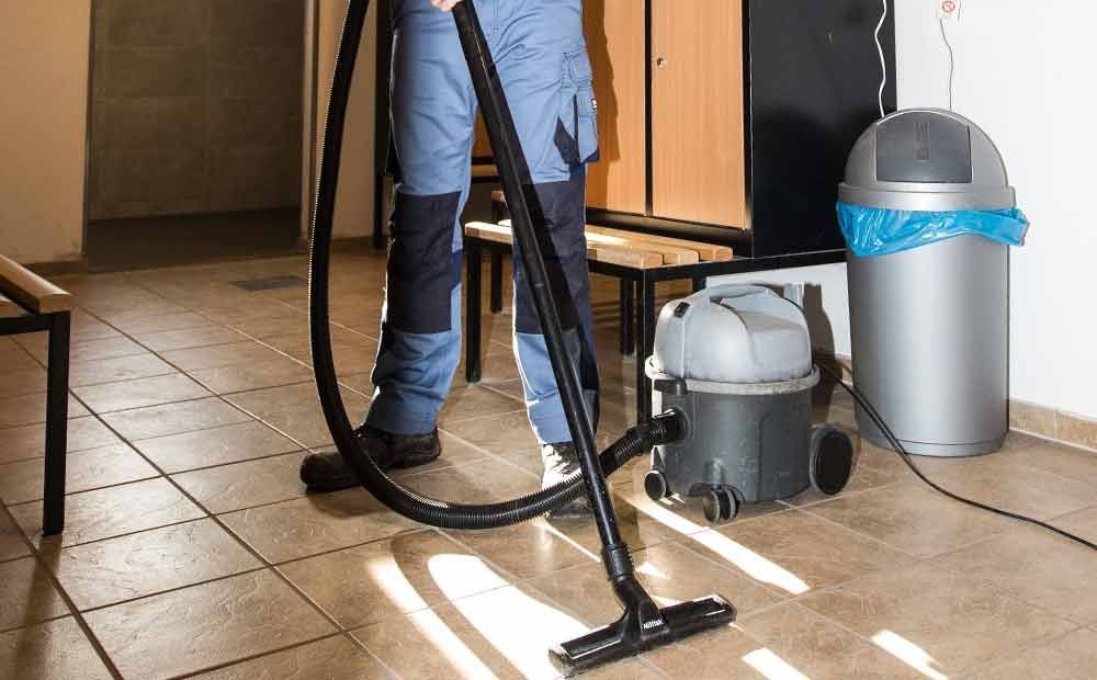 Eine Person reinigt einen Fliesenboden mit einem Staubsauger.