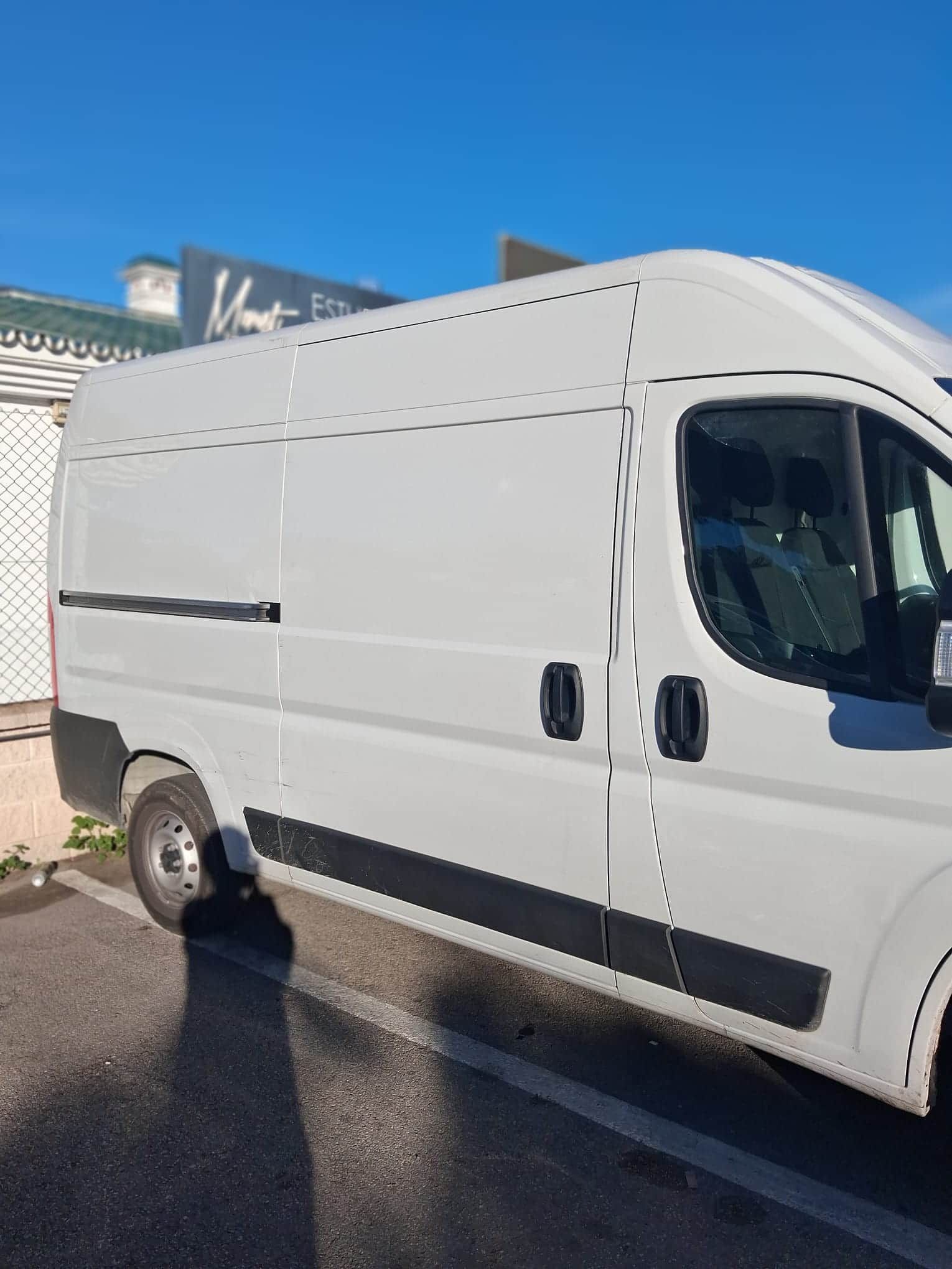 Furgoneta de carga blanca estacionada frente a un edificio en un día soleado.