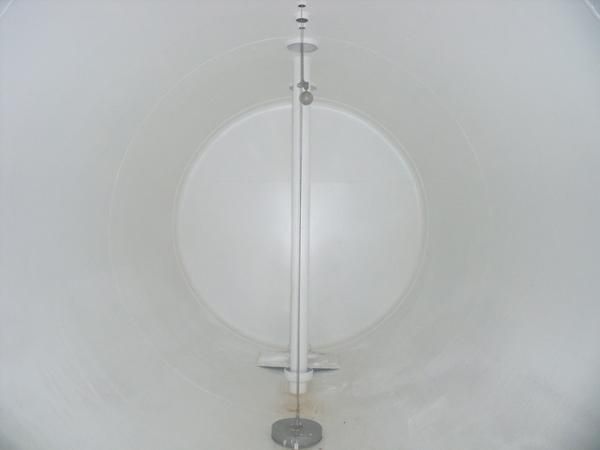 Dentro de un tanque blanco, una varilla vertical se extiende de arriba a abajo, con placas circulares unidas.