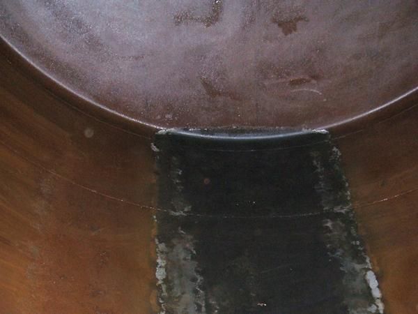 Interior oscuro de un recipiente curvo con una zona oscura y parcheada a lo largo del fondo.