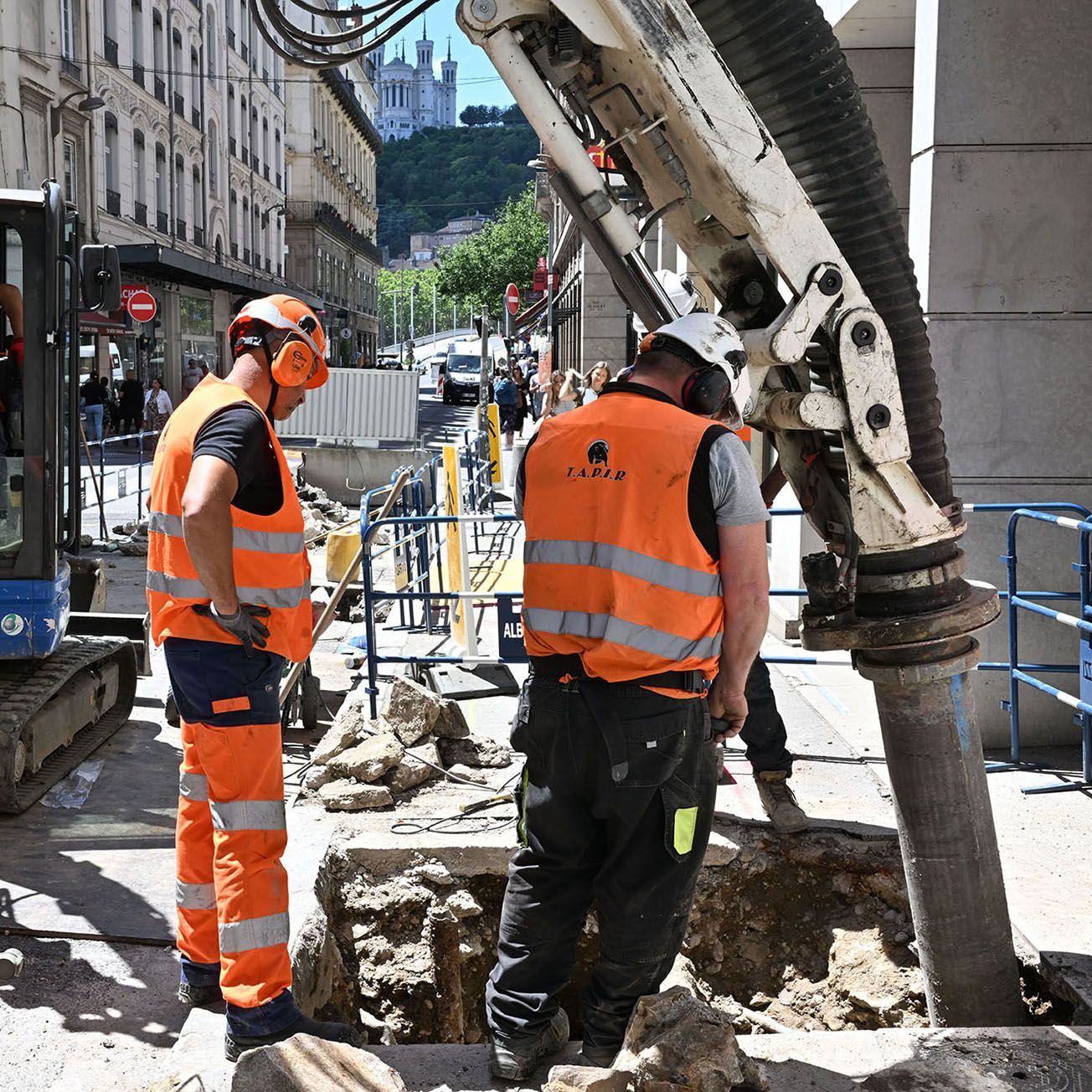 Travailleurs du BTP en gilet orange en train de surveiller une machine
