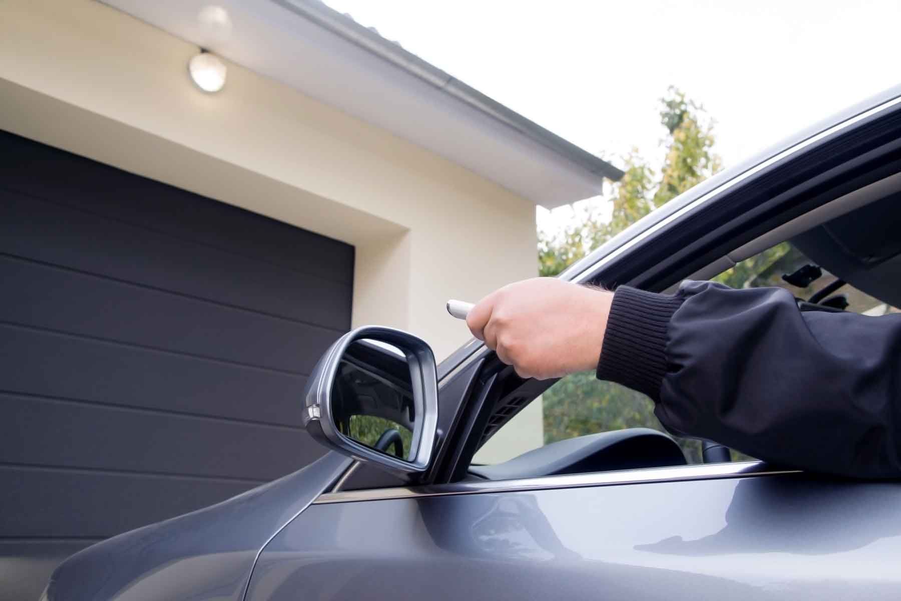 Un homme dans sa voiture actionne avec sa télécommande la porte de garage de son domicile