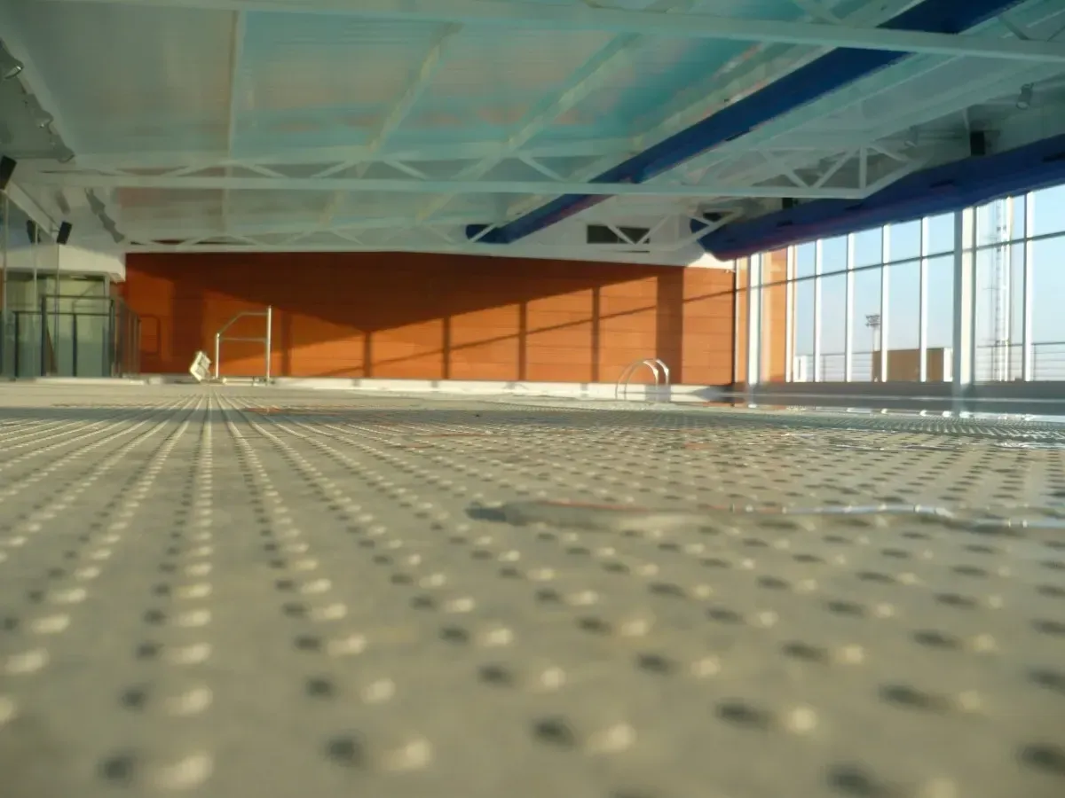 Piscina cubierta con suelo texturizado de color claro; luz solar en la pared y ventanas de color naranja.