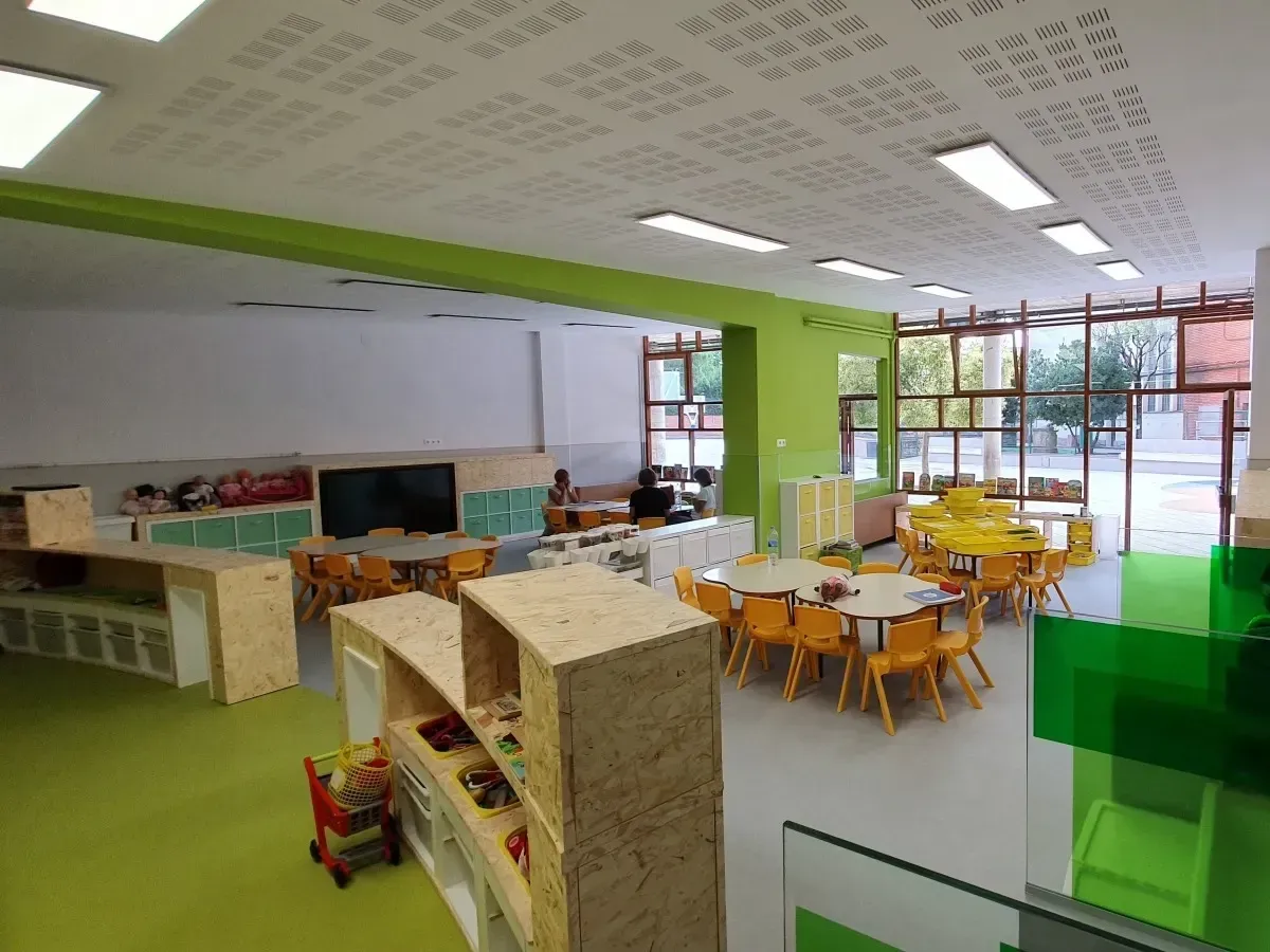 Aula bien iluminada con detalles en verde y blanco, mesas y estanterías abiertas.