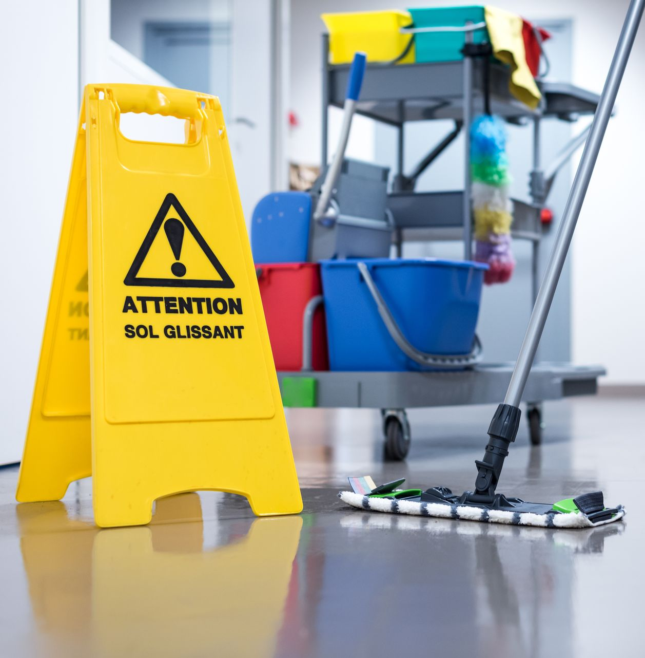 Panneau jaune sol glissant, chariot de nettoyage et serpillière sur un sol mouillé dans un couloir.