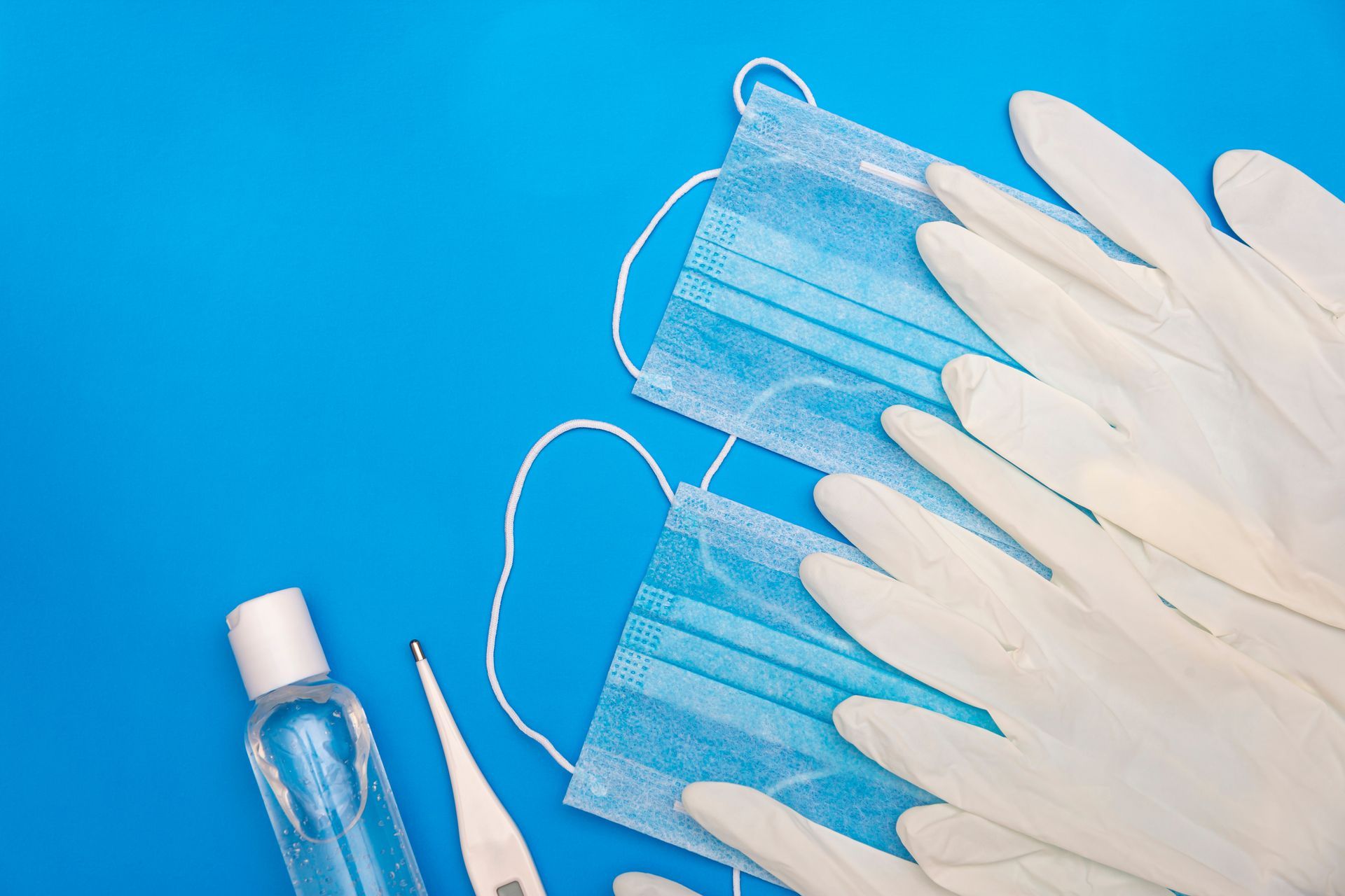 Masques médicaux bleus, gants, gel hydroalcoolique et thermomètre sur une surface bleue.