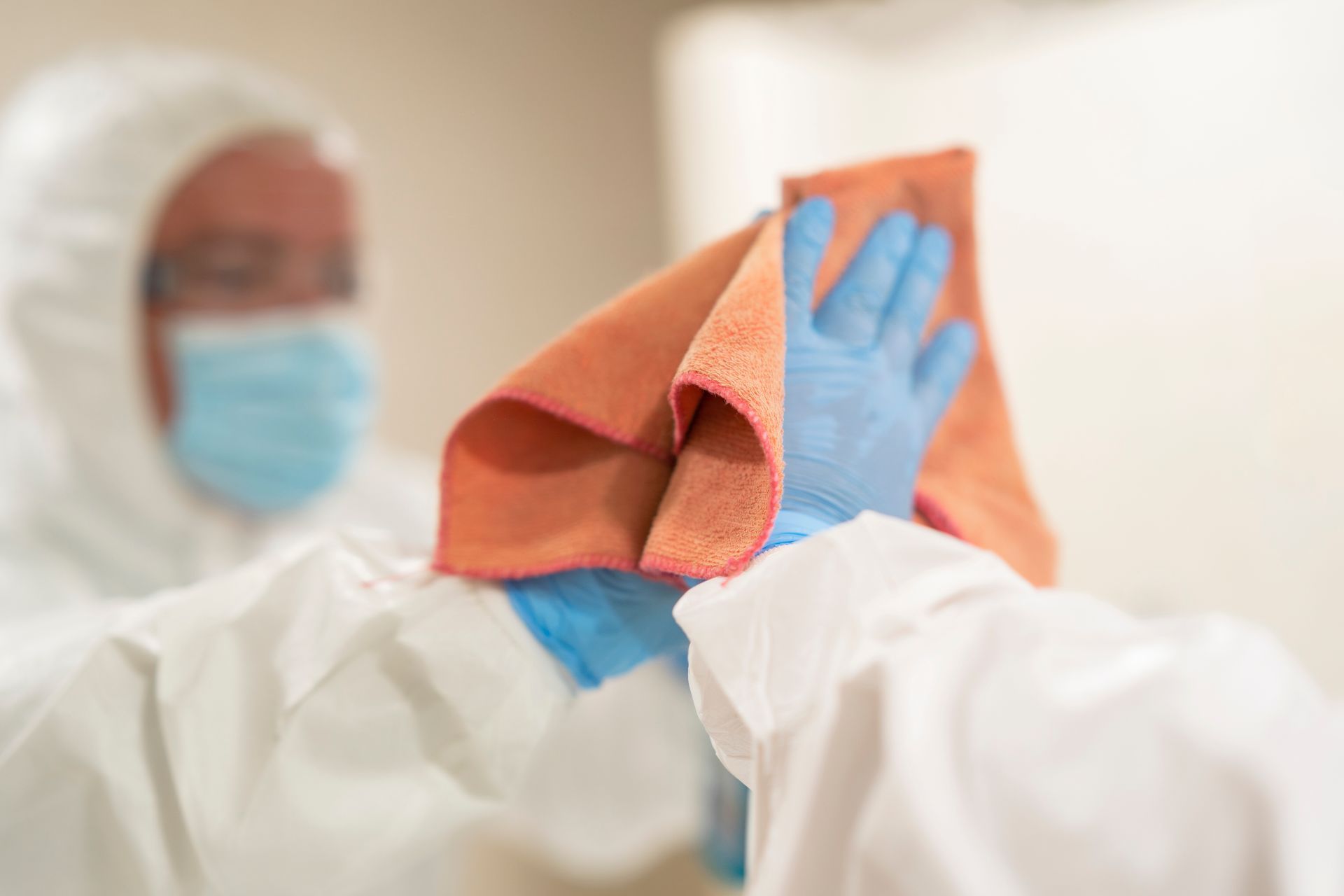Une personne portant une combinaison et un masque de protection nettoie une surface avec un chiffon en microfibre.