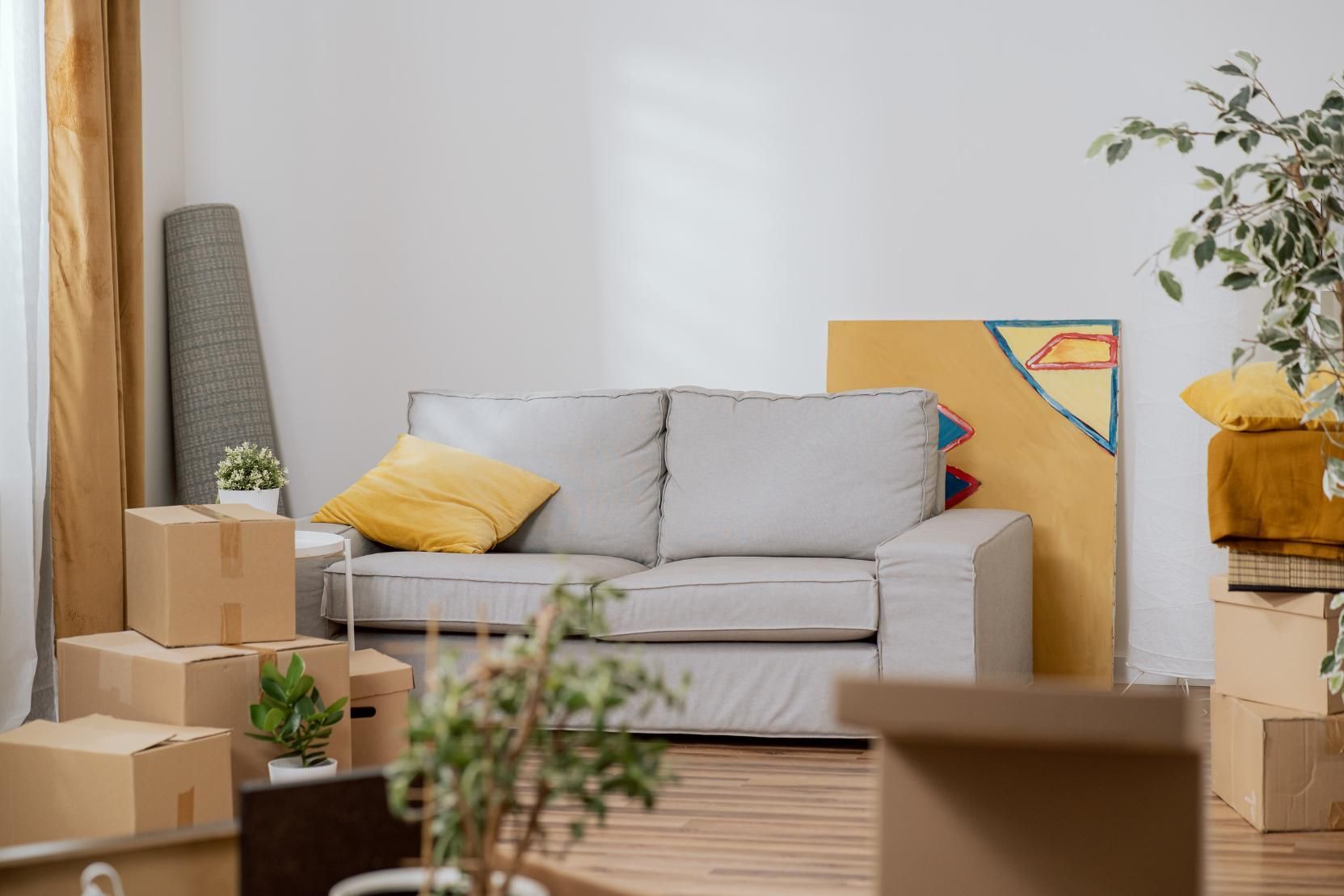 Unas cajas rodean un sofá gris claro en una habitación, lo que indica una mudanza. 