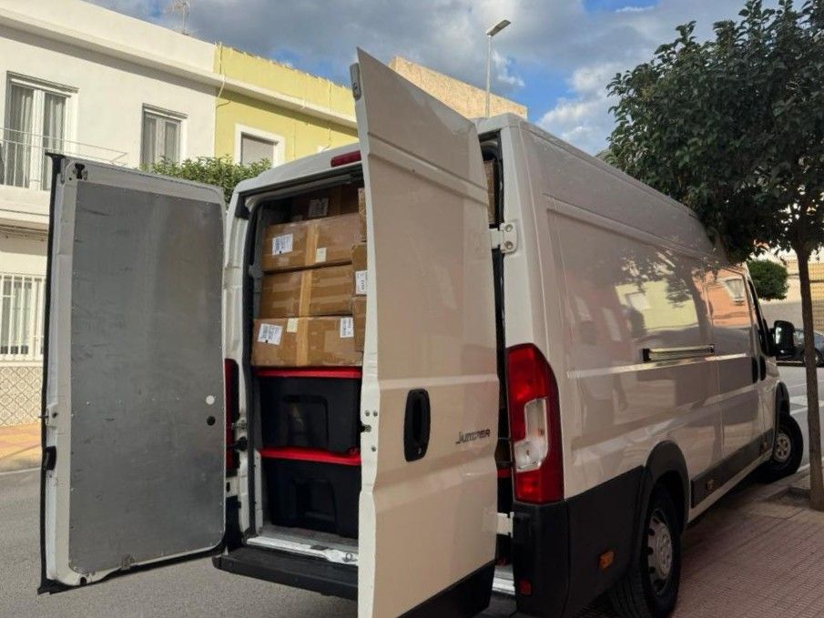 Furgoneta de reparto blanca estacionada en una calle con las puertas traseras abiertas dejando ver paquetes en su interior.