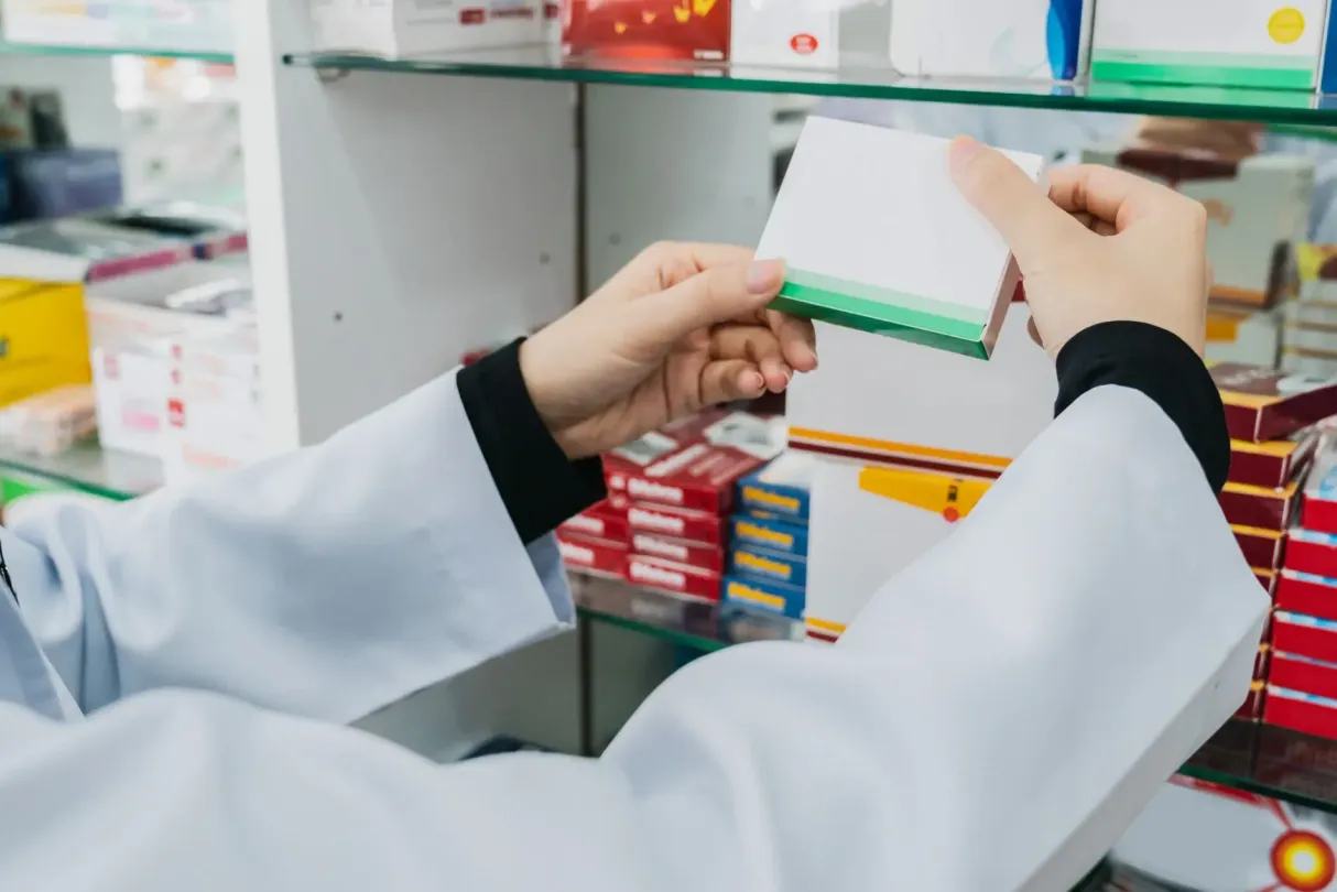 Un farmacéutico con bata blanca examina una caja de medicamentos en una farmacia.