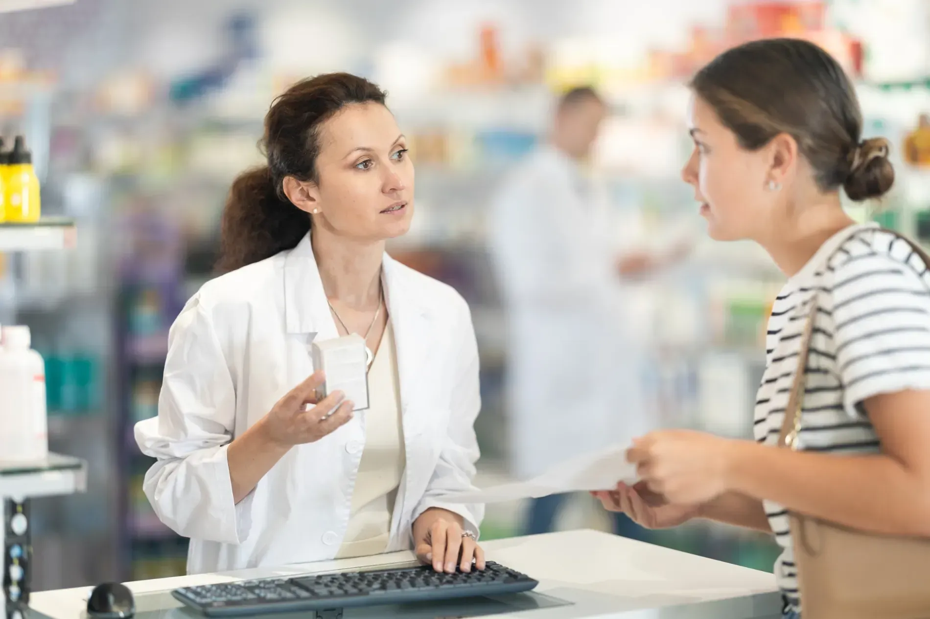 Un farmacéutico con bata blanca consulta con un cliente que tiene una receta en una farmacia.